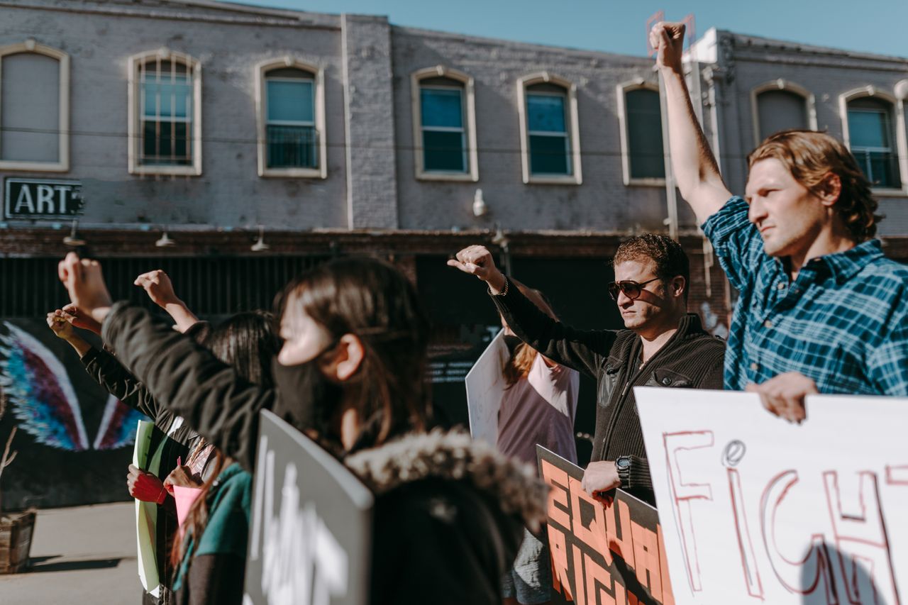 our-story A diverse group of protesters raise fists with placards demanding equal rights outdoors.