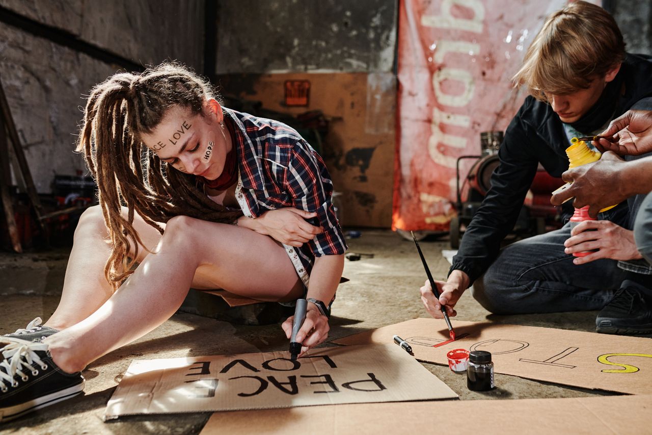 about-us Group of activists creating protest signs with paint on cardboard indoors, expressing peaceful messages.