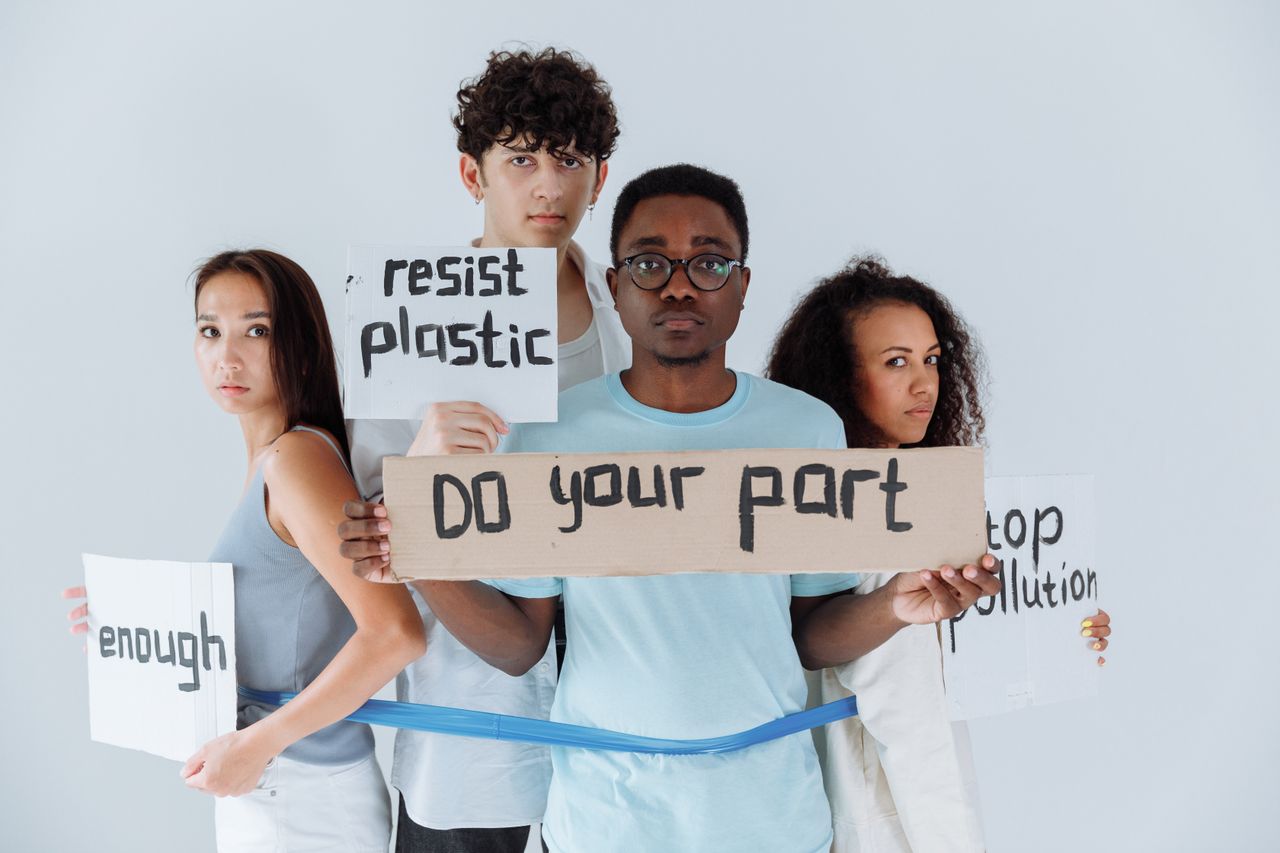 heros-img A diverse group of young adults holding signs promoting anti-plastic and pollution awareness.